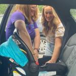 Child Passenger Safety Technician demonstrating how to install an infant car seat in the back seat of a passenger vehicle to a caregiver