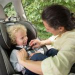 A mom works to secure an infant in a rear-facing car seat.