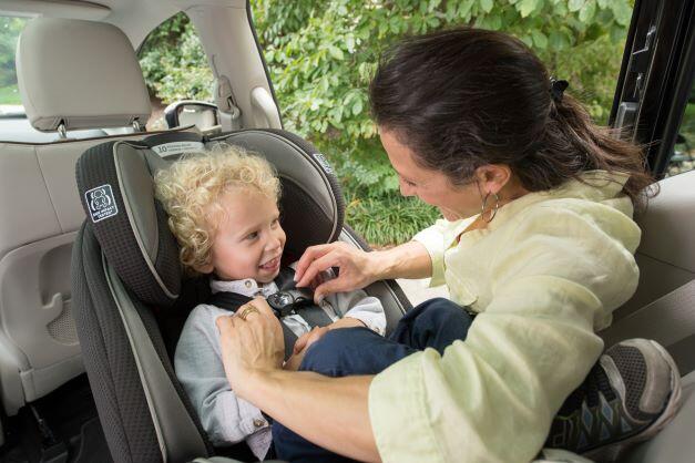 A mom works to secure an infant in a rear-facing car seat.