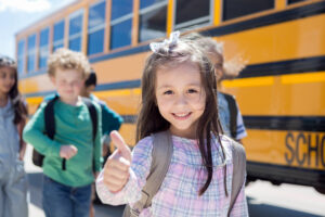 Image of a smiling child standing outside of a school bus